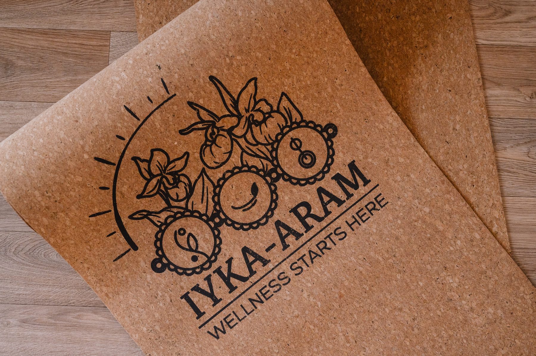 Close-up of an unrolled natural cork yoga mat printed with the Iyka-Aram logo and the words Wellness Starts Here