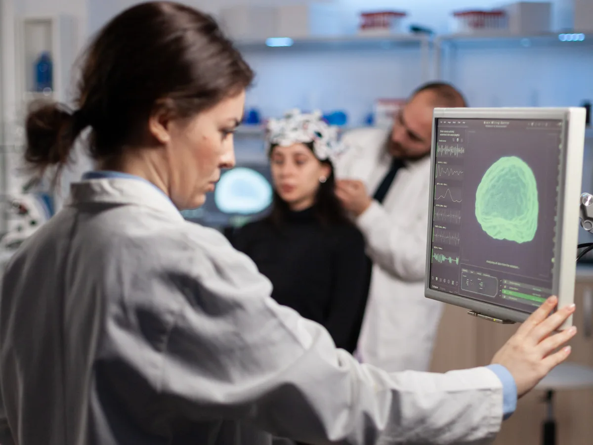Clinicians reading brain activity on a monitor while a patient wears an EEG cap