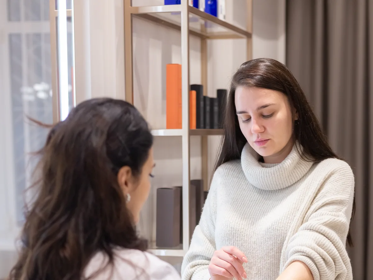 A clinician in a white coat examining a patient's forearm during a consultation