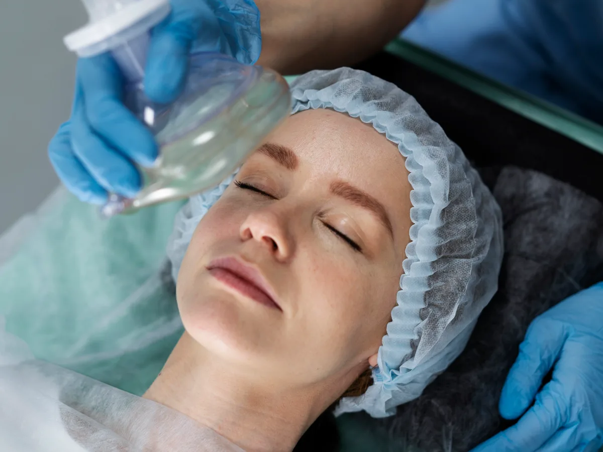 A nurse holding a breathing mask over a patient resting on a treatment couch