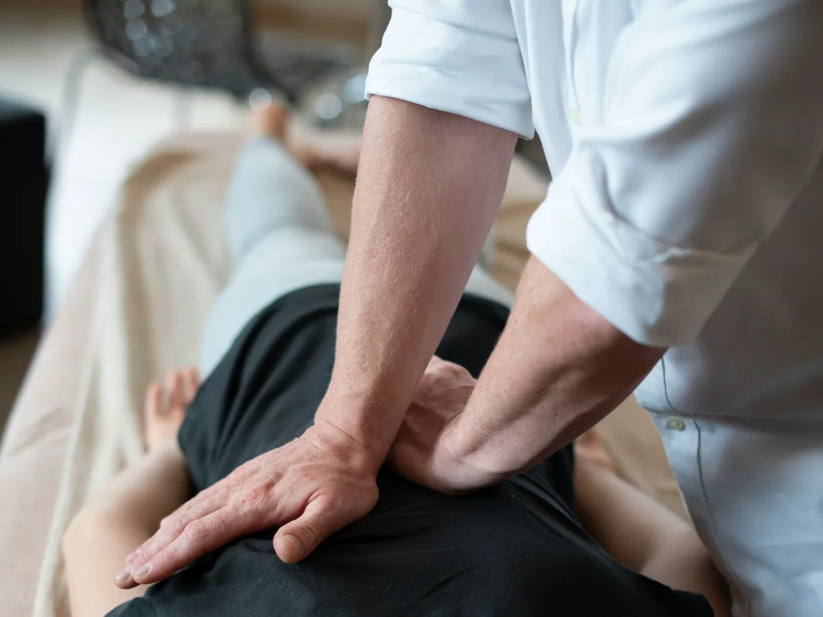 A physiotherapist applying pressure along a patient's spine on a treatment couch